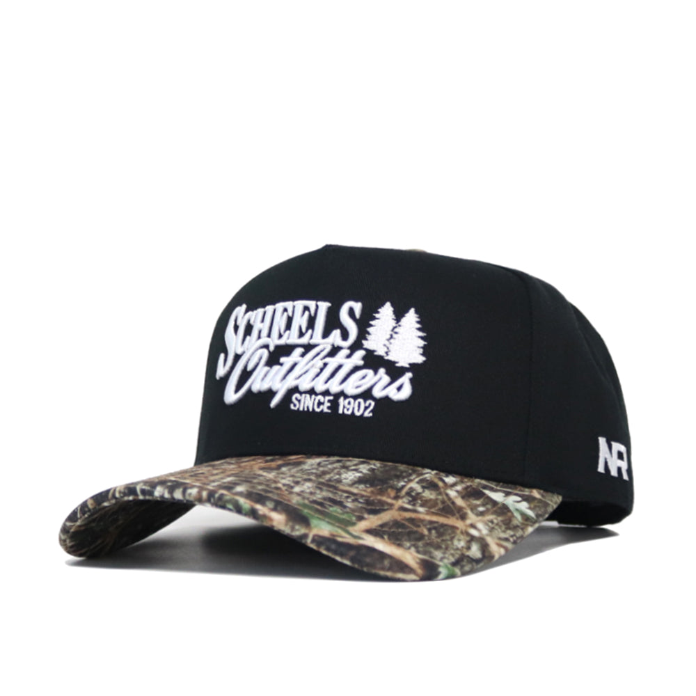 The Scheels Camo Trailblazer Hat is a black snapback with white embroidered text and two pine trees on the front, a camo-pattern brim, and a small white AF logo on the side. Made from high quality cotton with a structured fit.