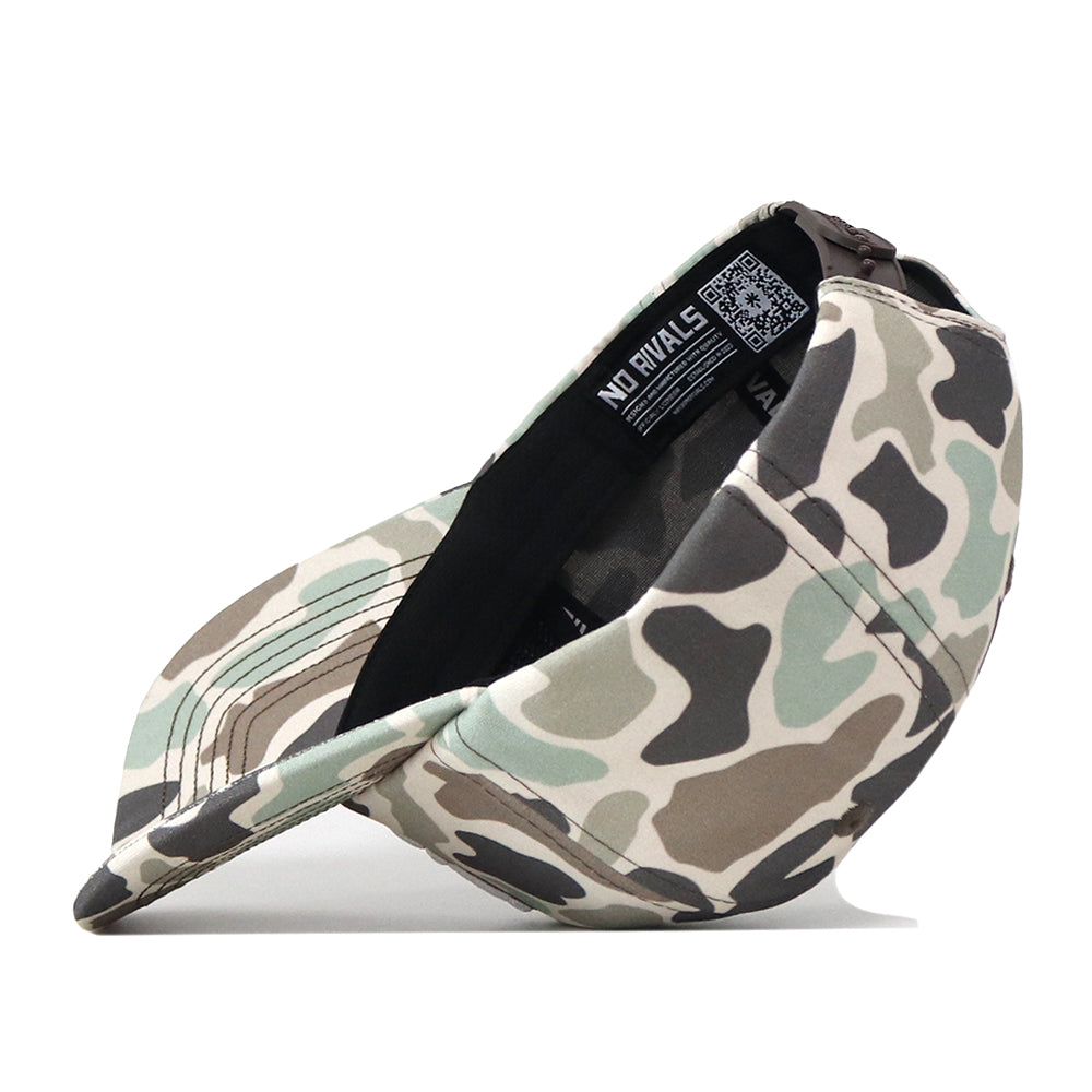 An Auburn Huntsman Hat by No Rivals, featuring a classic 5-panel design in duck camo, is displayed resting on its side with the inside label “NO RIVALS” visible near the back.