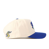 The South Dakota State Jackrabbits Stadium Hat by No Rivals is a cream snapback cap with a royal blue brim, showcasing an embroidered cartoon jackrabbit on the side along with blue-and-yellow embroidered logos on the front. This officially licensed hat delivers authentic style for fans.