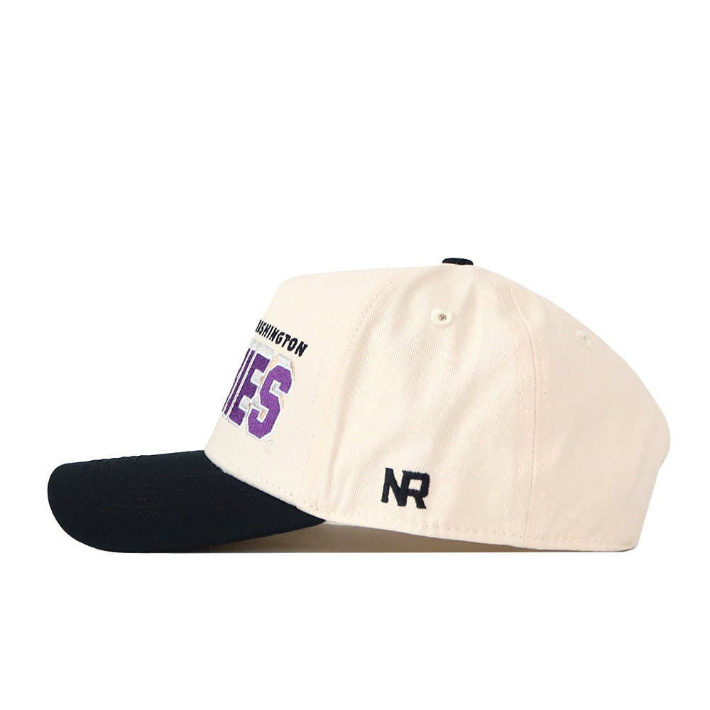 Side view of the Washington Huskies Alma Mater Hat by No Rivals, a cream-colored snapback cap with a black bill—ideal for topping off your gameday look. This hat displays black embroidered “NR” lettering on the side and features partially visible purple text on the front, showcasing its stylish No Rivals logos.