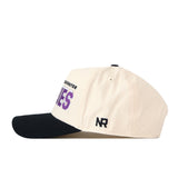 Side view of the Washington Huskies Alma Mater Hat by No Rivals, a cream-colored snapback cap with a black bill—ideal for topping off your gameday look. This hat displays black embroidered “NR” lettering on the side and features partially visible purple text on the front, showcasing its stylish No Rivals logos.