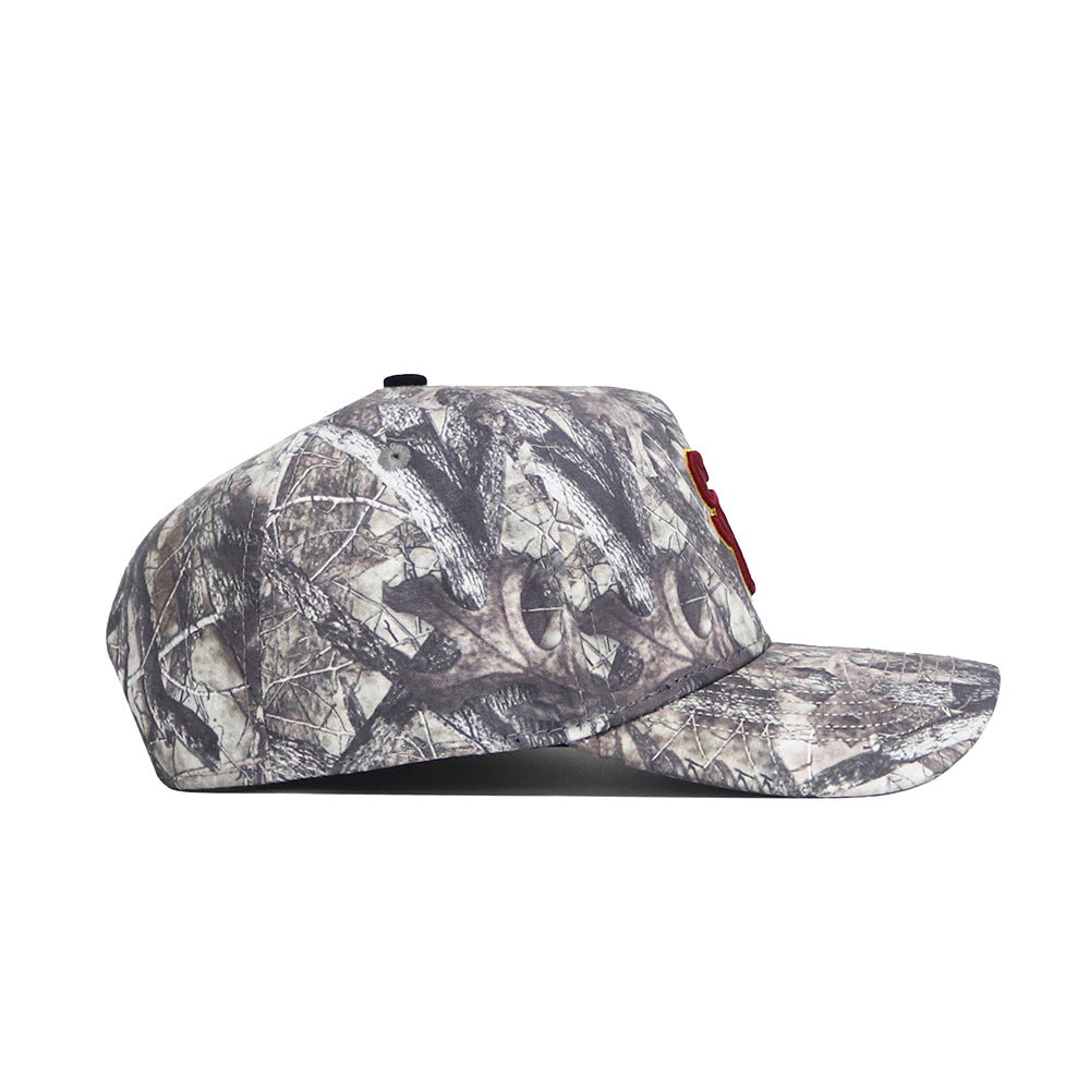 The USC Outland Hat by No Rivals is a structured snapback featuring a camouflage pattern in brown, grey, and black with natural, tree-like designs. Made from high-quality cotton and shown from the side.