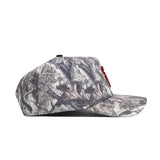 The USC Outland Hat by No Rivals is a structured snapback featuring a camouflage pattern in brown, grey, and black with natural, tree-like designs. Made from high-quality cotton and shown from the side.
