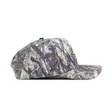 A side view of the No Rivals South Dakota State Outland Hat, a flat-brim snapback with a forest camo pattern featuring tree branches and leaves in brown, green, and gray. Made from high-quality cotton with a structured fit.