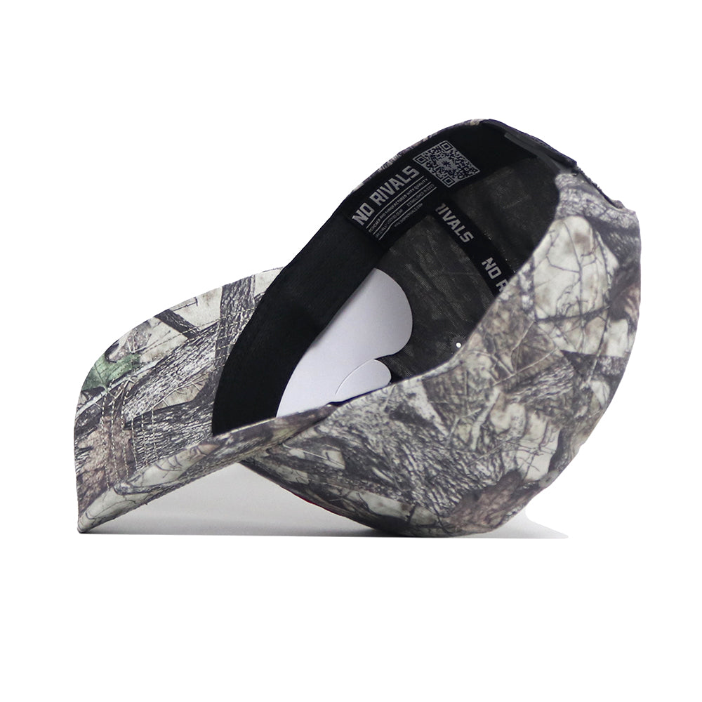 The UConn Outland Hat by No Rivals is a camouflage baseball cap shown side-on, with the brim left and its high-quality cotton, black interior featuring "NO RIVALS" text on the band clearly visible.