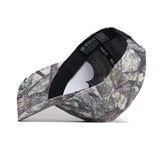 The UConn Outland Hat by No Rivals is a camouflage baseball cap shown side-on, with the brim left and its high-quality cotton, black interior featuring "NO RIVALS" text on the band clearly visible.