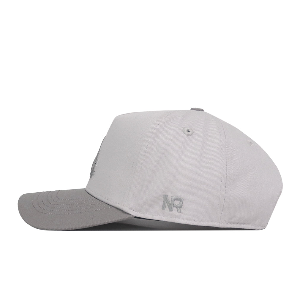 The UNT Graphite Hat by No Rivals is displayed in a left side view, showcasing its light gray color with a subtly darker brim. The hat features an embroidered NR logo near the back and includes a Snap Back Adjustment for a personalized fit.