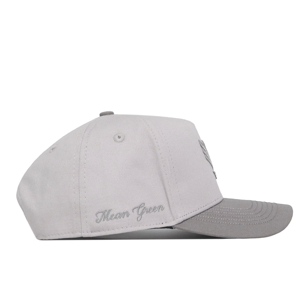 A light gray UNT Graphite Hat by No Rivals is shown from the side, featuring “Mean Green” embroidered in cursive near the back. The hat includes a curved bill, visible stitching, and a convenient Snap Back Adjustment for a customized fit.
