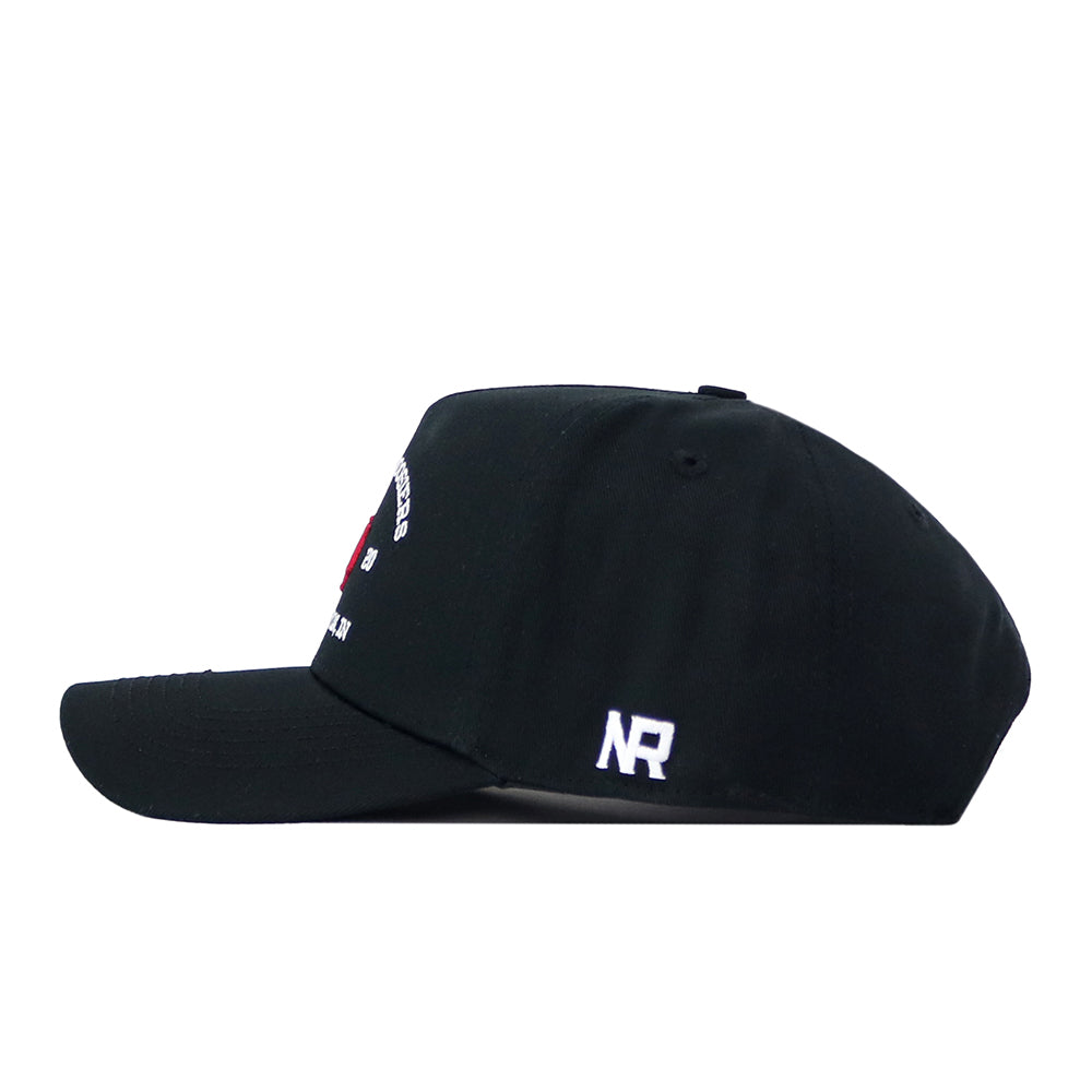 The Indiana Outlaw Hat - Black by No Rivals is displayed from the side, showcasing a small white NR embroidered logo. This cap features a flat brim, a structured crown, and a classic snap back closure for an adjustable fit.