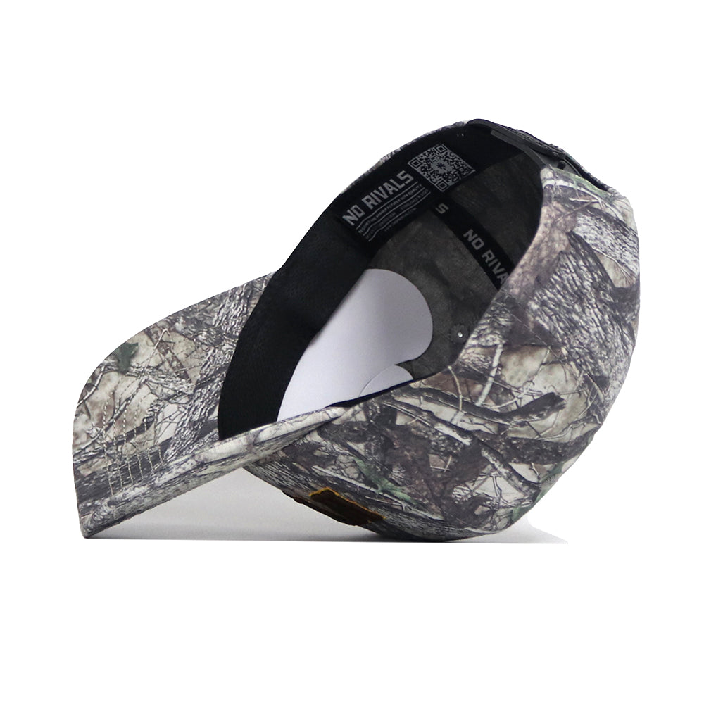 The Wyoming Outland Hat by No Rivals is pictured upside down, showing its black sweatband and NO RIVALS label. The snapback features a forest-inspired camouflage pattern on high-quality cotton brim and panels.