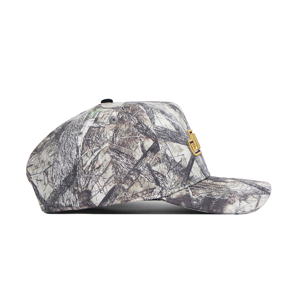 A side view of the No Rivals JMU Outland Hat, featuring a camouflage pattern, small gold emblem, and flat brim. Made from high-quality cotton, the cap is shown against a plain white background.