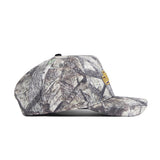 A side view of the No Rivals JMU Outland Hat, featuring a camouflage pattern, small gold emblem, and flat brim. Made from high-quality cotton, the cap is shown against a plain white background.