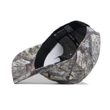 The JMU Outland Hat by No Rivals is a high quality cotton baseball cap in a woodland green and brown camouflage pattern, shown on its side to display the underside brim and interior band with "NO RIVALS" printed inside.