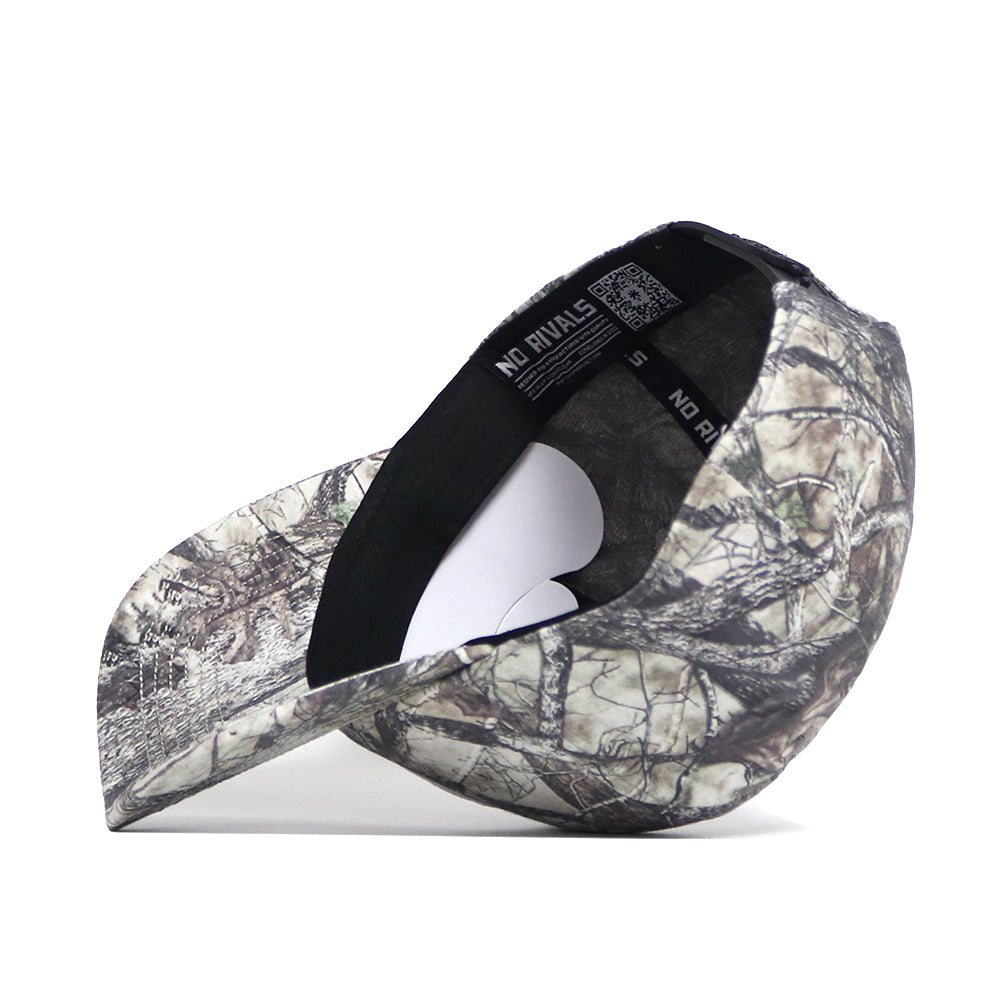 The No Rivals Colorado State Outland Hat is displayed upside down, showing its black sweatband and label. Its structured fit exterior sports a forest camo pattern with branches and leaves.