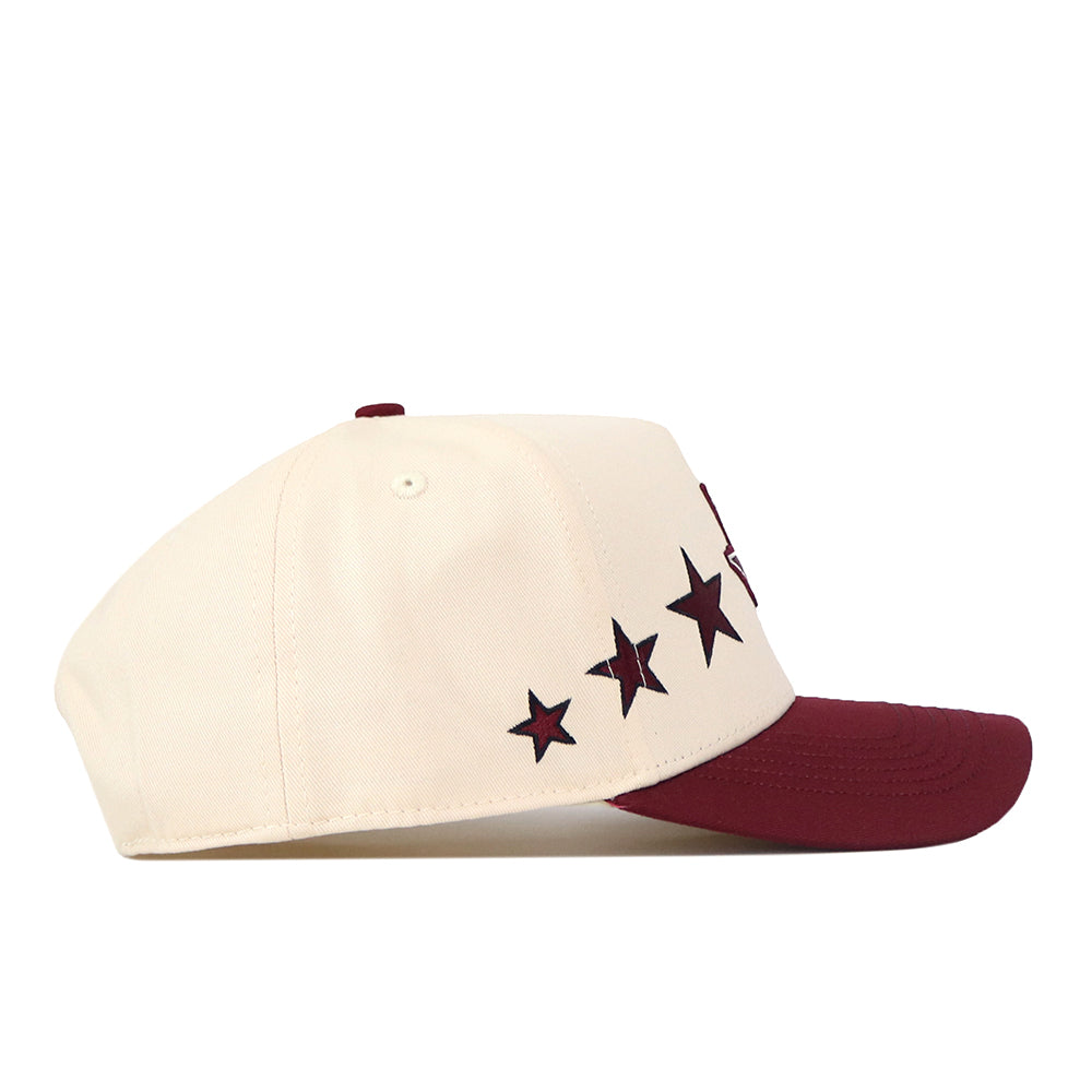 Introducing the Texas A&M Star Hat by No Rivals—a cream-colored snapback baseball cap with a maroon brim, five black stars along the side, and an officially licensed embroidered logo for a stylish, authentic touch.