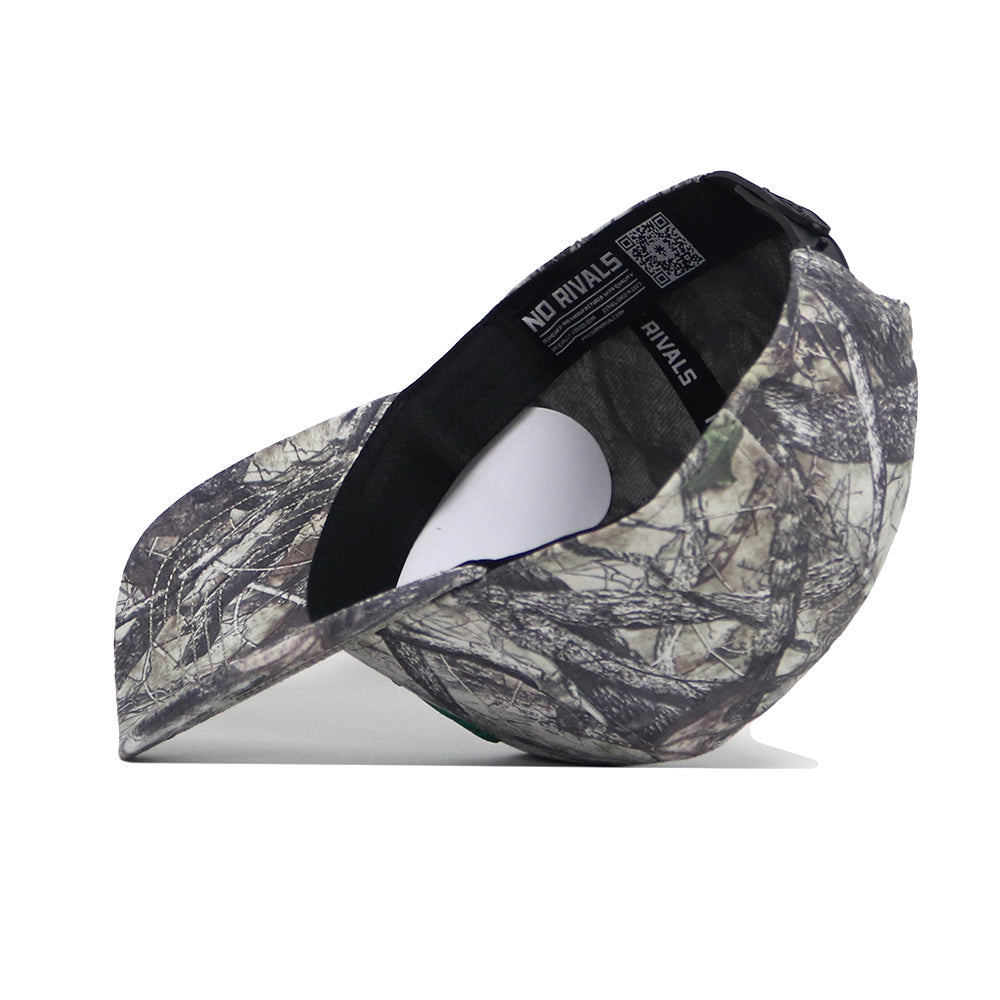 The North Texas Outland Hat by No Rivals is a high-quality cotton snapback with a green, brown, and gray camouflage pattern. Pictured on its side with the brim left, it features an inside label reading NO RIVALS.