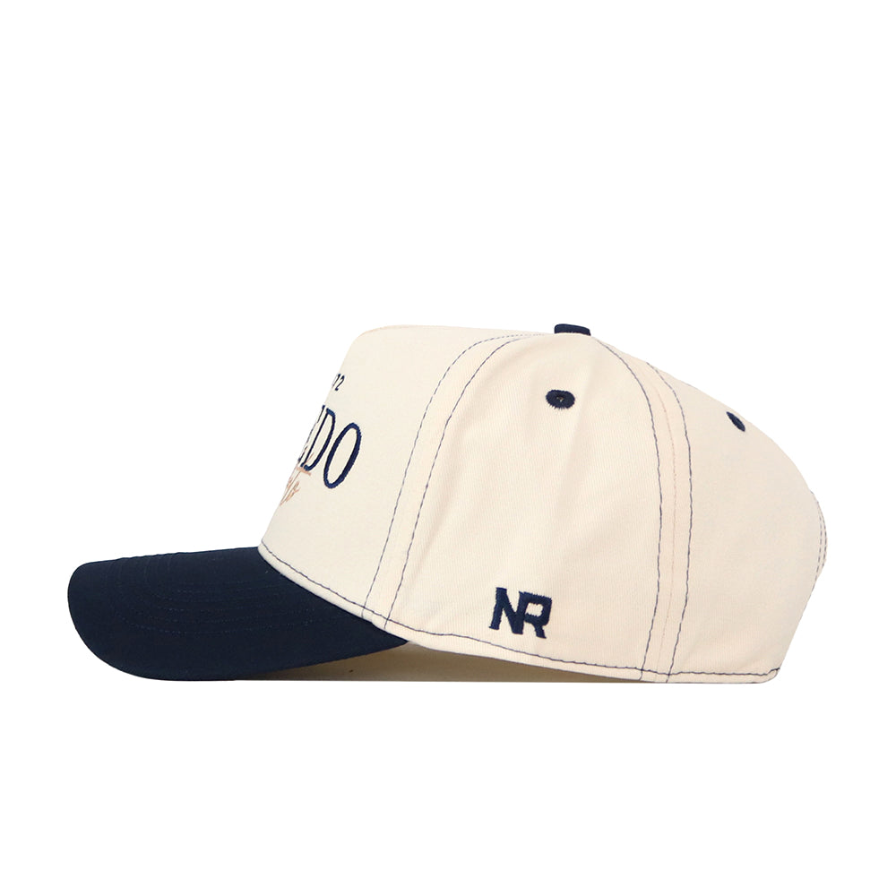 A beige Toledo Rockets Vintage Hat by No Rivals features a navy blue brim, navy stitching, and the initials “NR” embroidered in navy on the side, along with an officially licensed embroidered logo for a touch of authenticity.