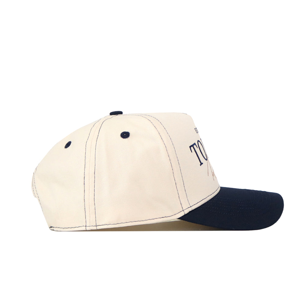 The No Rivals Toledo Rockets Vintage Hat is shown from a side view, showcasing its cream-colored crown and navy blue brim. Visible stitching, two ventilation holes on the side panel, and a partially seen embroidered logo on the front add to its authentic look. This officially licensed snapback blends classic style with signature team details.