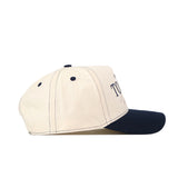The No Rivals Toledo Rockets Vintage Hat is shown from a side view, showcasing its cream-colored crown and navy blue brim. Visible stitching, two ventilation holes on the side panel, and a partially seen embroidered logo on the front add to its authentic look. This officially licensed snapback blends classic style with signature team details.
