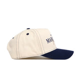 The No Rivals Marquette Vintage Hat is a beige structured snapback with a navy blue brim, stitching, and eyelets. Made from quality cotton, it features "MAR" and a small graphic on the front. Shown side view on white background.