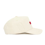 The Georgia Sideline Hat by No Rivals is a beige baseball cap with a small red embroidered front design, crafted from high-quality cotton with visible stitching, ventilation eyelets, and a comfortable fit.