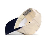 The Marquette Vintage Hat by No Rivals is a cream and navy snapback shown flipped to display inner labels, NO RIVALS text on the inner band, structured fit, and visible crown seams.