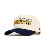 The No Rivals Marquette Alma Mater Hat is a beige and navy snapback made from high-quality cotton, featuring "GOLDEN EAGLES MARQUETTE" embroidered in yellow/navy and an R logo on the side. Officially licensed.
