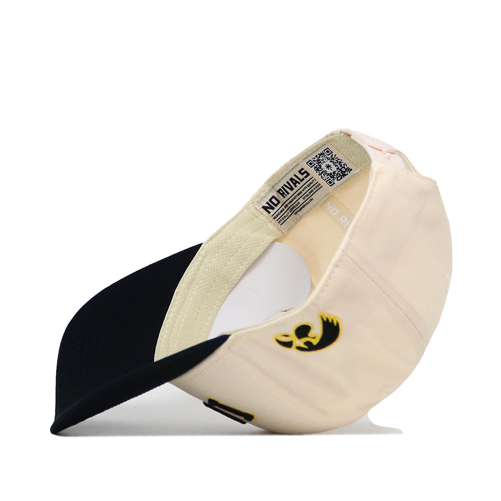 The Right Side Up Iowa Hat - Classic by No Rivals is shown upside down, revealing its inside label with a QR code and the signature NO RIVALS text. This cream and black snapback features a small embroidered black-and-gold logo near the adjustable strap opening—perfect for elevating your gameday style.