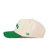 Introducing the Right Side Up Marshall Hat by No Rivals—a cream baseball cap featuring a green brim. The side is adorned with green embroidered "NR" lettering, showcasing the stylish No Rivals logo. Designed for comfort and style, this structured hat includes ventilation eyelets and contrast stitching on the brim for added detail.