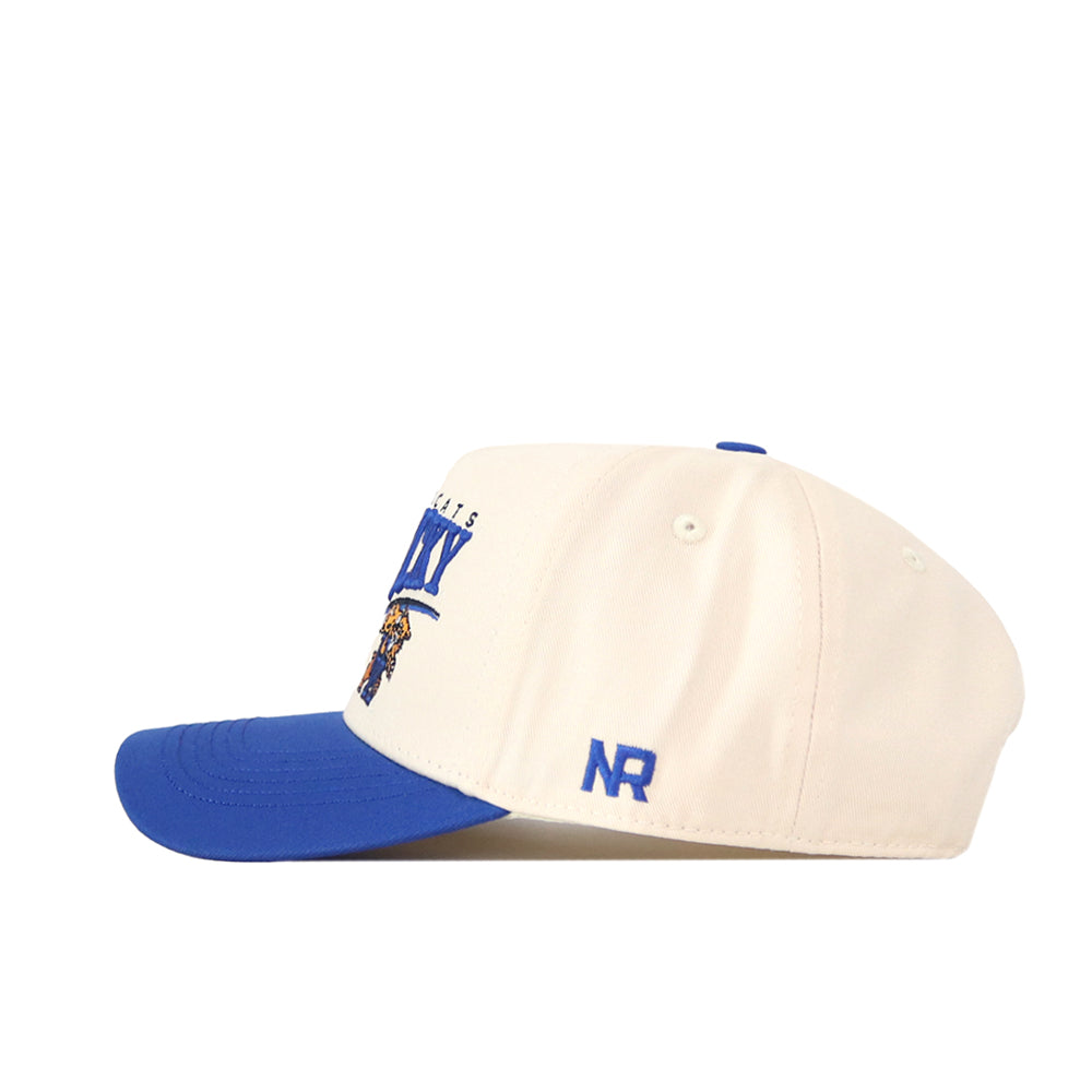 A cream Kentucky Wildcats Stride Hat by No Rivals, featuring a blue brim, blue "NR" initials on the side, and a graphic with text on the front. Made from high-quality cotton for comfort and durability, this structured fit cap is displayed from a side view against a white background.