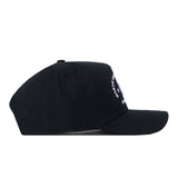 A side view of the UNC Outlaw Hat in black by No Rivals, featuring a structured fit and an embroidered logo on the front. The cap displays minimal visible details, with some white text and graphics partially shown for added style.