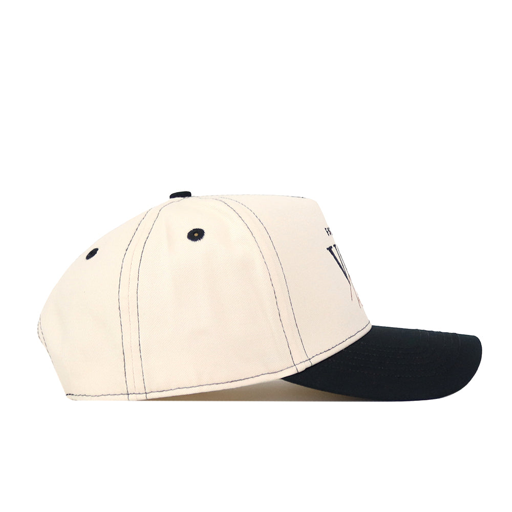 Side view of the No Rivals VCU Rams Vintage Hat, a two-tone snapback baseball cap with a cream crown and black brim, featuring dark contrast stitching and a partially embroidered VCU Rams logo on the front panel—perfect for your next gameday fit.
