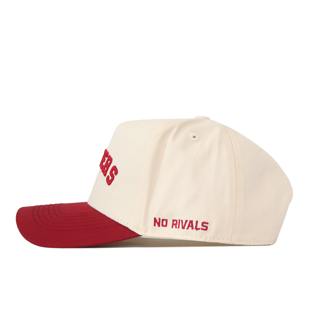 A side view of the Right Side Up Hoosiers Hat - Classic Colors by No Rivals, featuring a cream-colored snapback design with a red brim. “NO RIVALS” and an embroidered logo are stitched in red near the back.