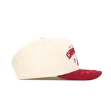 The Alabama Rally Hat by No Rivals is a cream snapback made from premium cotton, featuring a red brim and front embroidery. Displayed in side view against a white background.