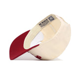 The Alabama Rally Hat by No Rivals is a cream snapback with a red brim, shown upside down to reveal the inside label reading NO RIVALS. Made from high-quality cotton, it includes an embroidered logo, QR code, and adjustable strap.