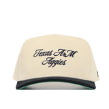The No Rivals Texas A&M Traditions Hat is cream corduroy with "Texas A&M Aggies" in black script, a structured fit, black brim with green underside, and an adjustable snapback.