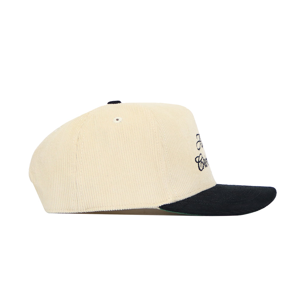 The Alabama Traditions Hat by No Rivals is a cream corduroy snapback with a black brim and structured fit. Black embroidered text decorates the front panel, shown from the side against a white background.