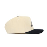 The Alabama Traditions Hat by No Rivals is a cream corduroy snapback with a black brim and structured fit. Black embroidered text decorates the front panel, shown from the side against a white background.