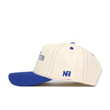The Creighton Vintage Hat by No Rivals features a cream cotton body, blue brim, blue stitching, and "NR" embroidered on the side in blue. Photographed against a white background.