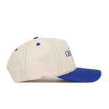 Side view of the Creighton Vintage Hat by No Rivals—a cream-colored baseball cap with blue stitching, a blue top button and curved brim, structured fit, and partially visible embroidered text on the front.