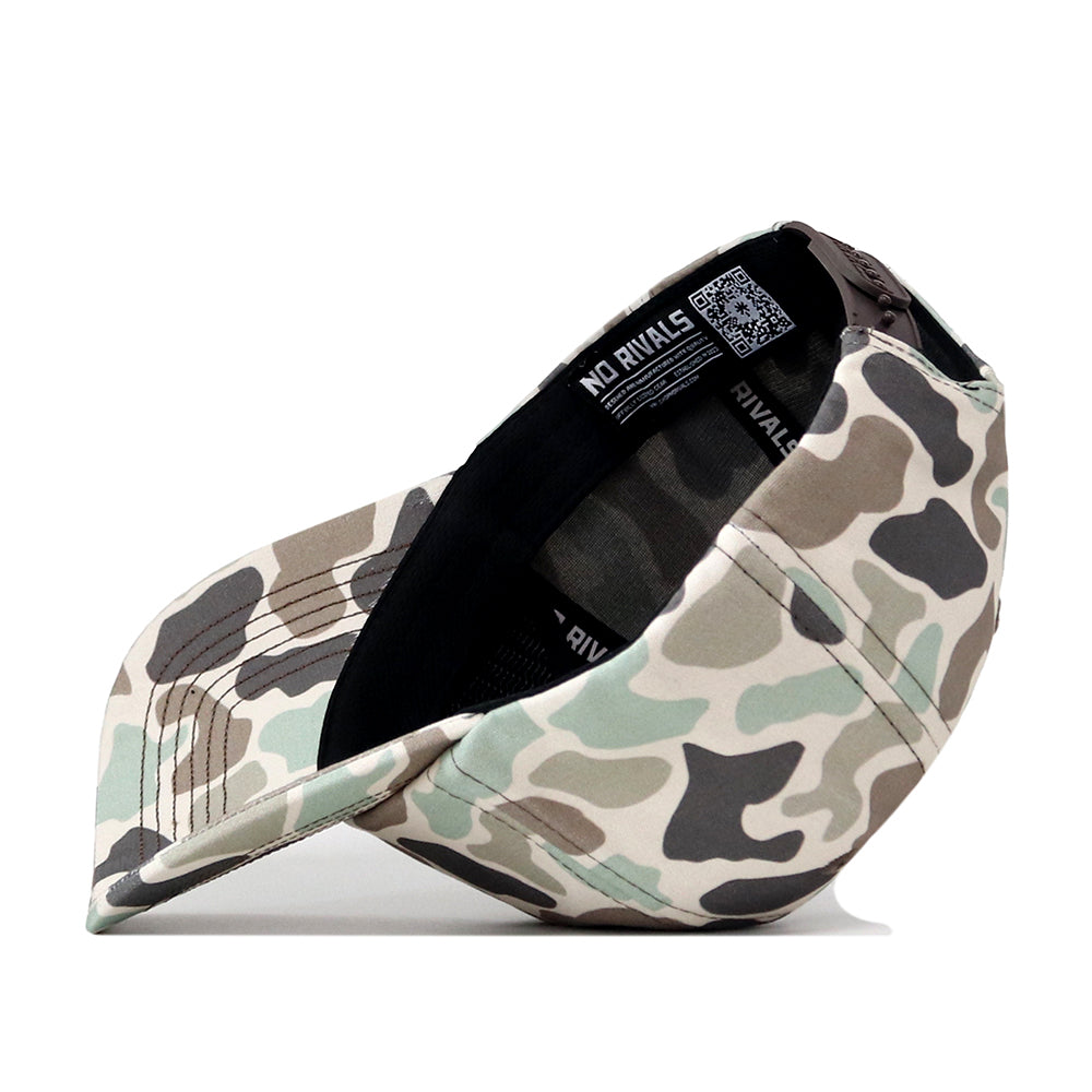 The Texas State Huntsman Hat by No Rivals is showcased upside down to reveal its black interior and label details. The exterior displays a green, brown, and beige camo pattern with an embroidered logo on the front—perfect for completing your Gameday Fit.