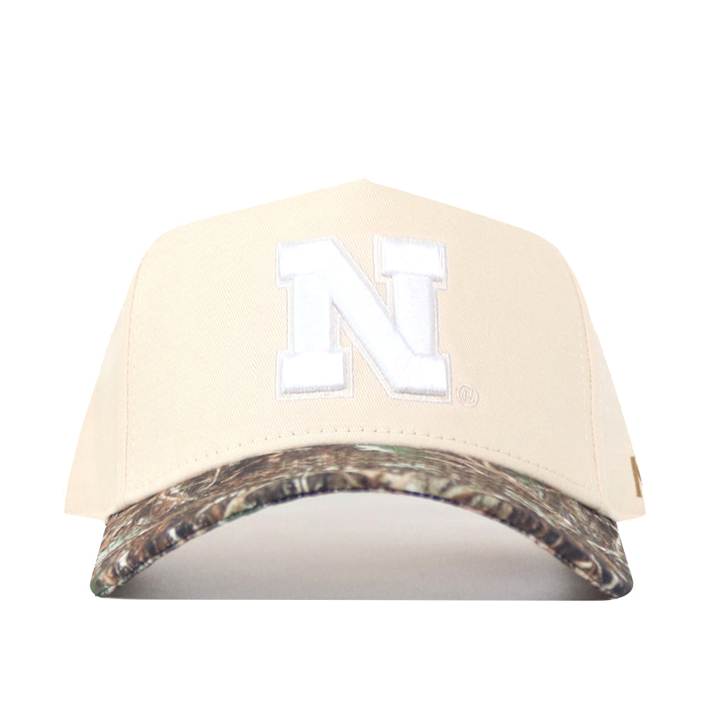 Introducing the Nebraska Camo Hat - Connector Edition by No Rivals: a high-quality cotton beige baseball cap with a white “N” on the front and a camouflage-patterned brim, displayed against a white background.
