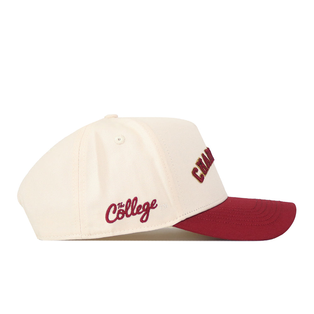 A cream-colored snapback hat with a maroon brim from No Rivals. The Right Side Up Charleston Hat - Classic features the College’s officially licensed embroidered logo in maroon on the side, with partial letters visible on the front.