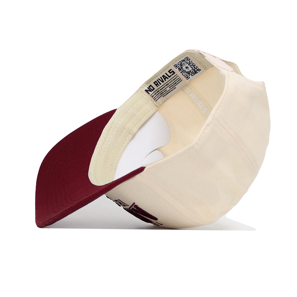 The Texas A&M Rally Hat by No Rivals is a cream snapback with a maroon brim, shown from the underside to highlight its inner label, stitching, and premium cotton. The cap displays “NO RIVALS” inside.