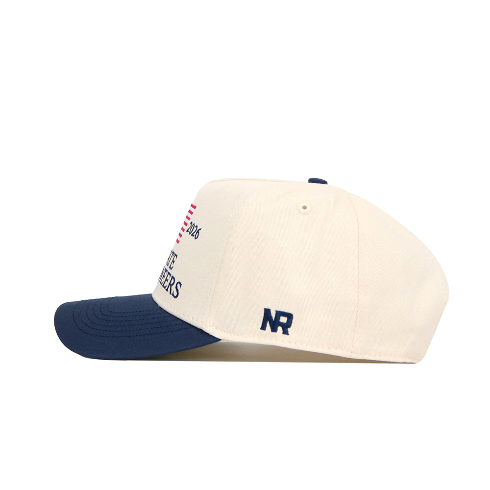 The No Rivals App State Mountaineers 250th Americana Hat is a cream snapback with a navy brim, an embroidered NR logo on the side, partial text and a small American flag on the front panel.