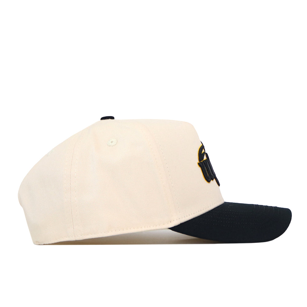 The Wichita State Patch Hat by No Rivals is a beige snapback with a black curved brim, black top button, and high-quality cotton. A front embroidered design is partially visible from the side view.