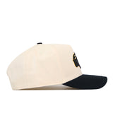 The Wichita State Patch Hat by No Rivals is a beige snapback with a black curved brim, black top button, and high-quality cotton. A front embroidered design is partially visible from the side view.