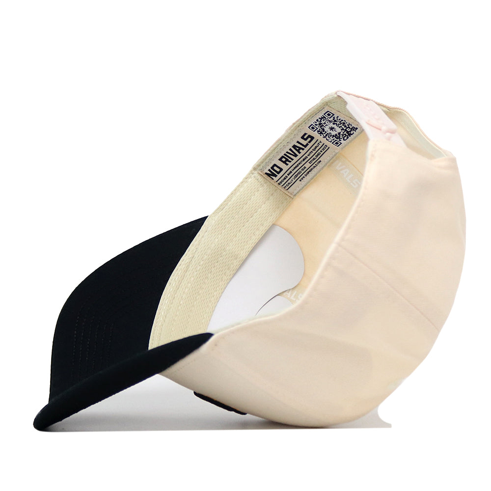 The Wichita State Patch Hat by No Rivals is shown upside down, revealing its label. This beige and black cotton snapback features a curved bill and visible stitching.