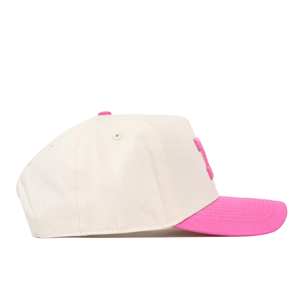 The No Rivals Michigan Pink Out Hat is a beige baseball cap featuring a pink brim and a matching pink button on top. Displayed in a side profile view against a plain white background, this officially licensed breast cancer awareness hat offers an adjustable snap back for customizable comfort.