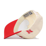 The Right Side Up Nebraska Hat - Classic by No Rivals is shown upside down, revealing its interior and a label reading "NO RIVALS." This beige snapback cap features a red bill and a red embroidered letter N on the side. Made from high-quality cotton, it offers both comfort and durability.